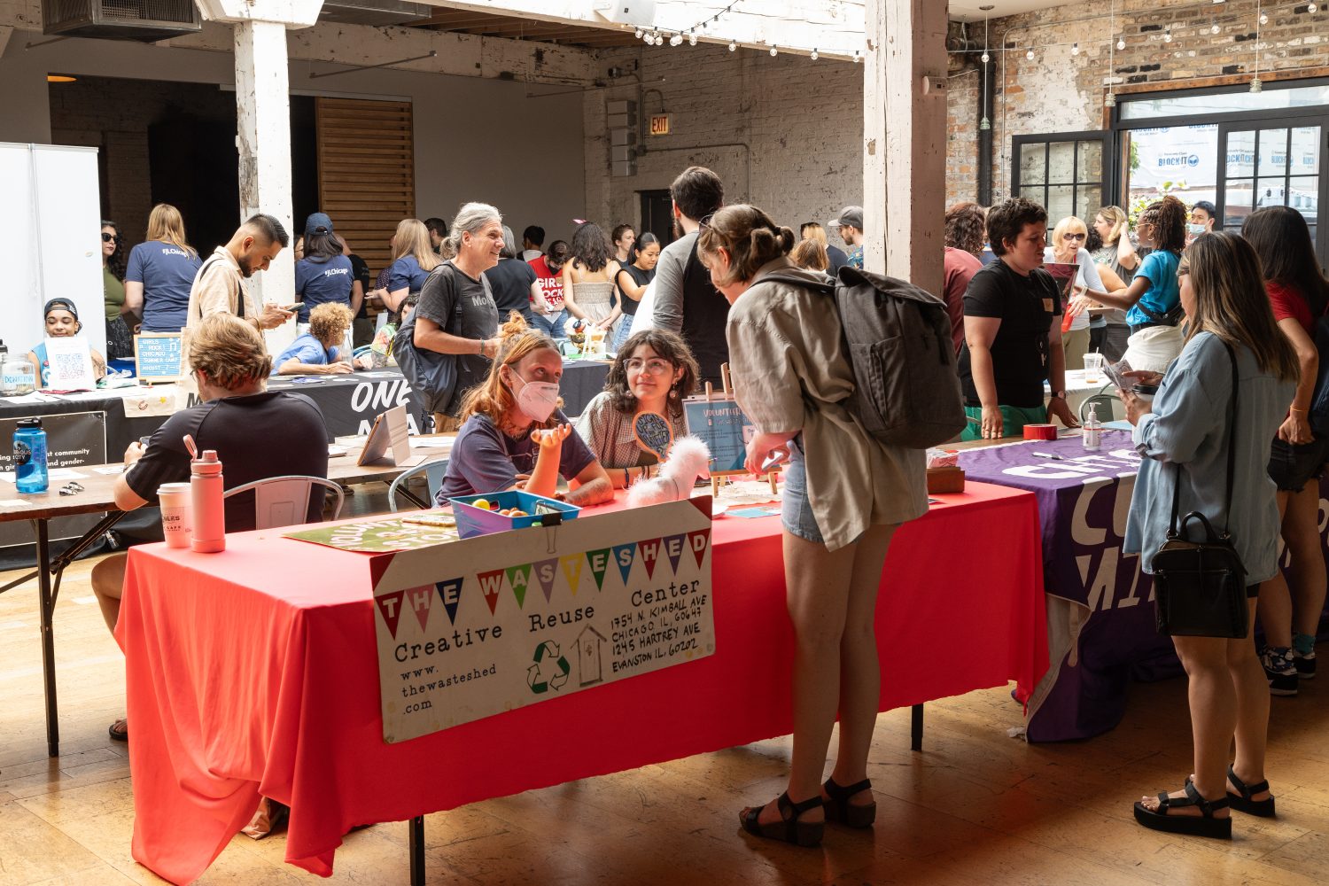 people sitting at tables with colored table cloths and signs, people standing on other side