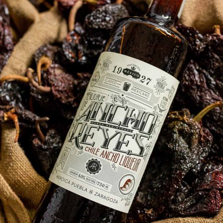 A bottle of Ancho Reyes Original liqueur on a bed of chiles