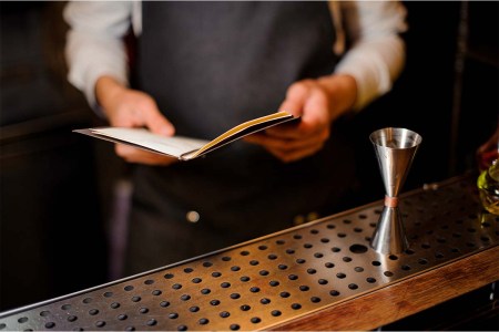 Bartender standing on the bar counter with a recipe book ready to preparing an alcoholic summer cocktail