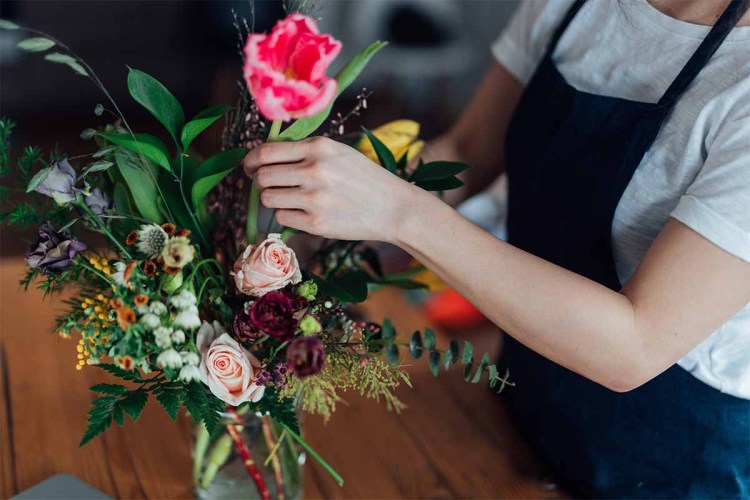 Cropped shot of young beautiful woman arranging fresh flowers in her living room.