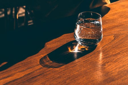 A glass of sparkling water standing on a sunlit wooden table casting shadows and lens flare