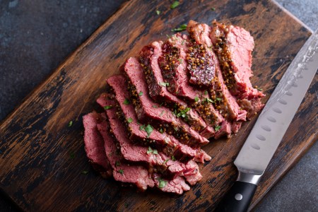 Corned beef cooked and sliced on a cutting board next to a knife