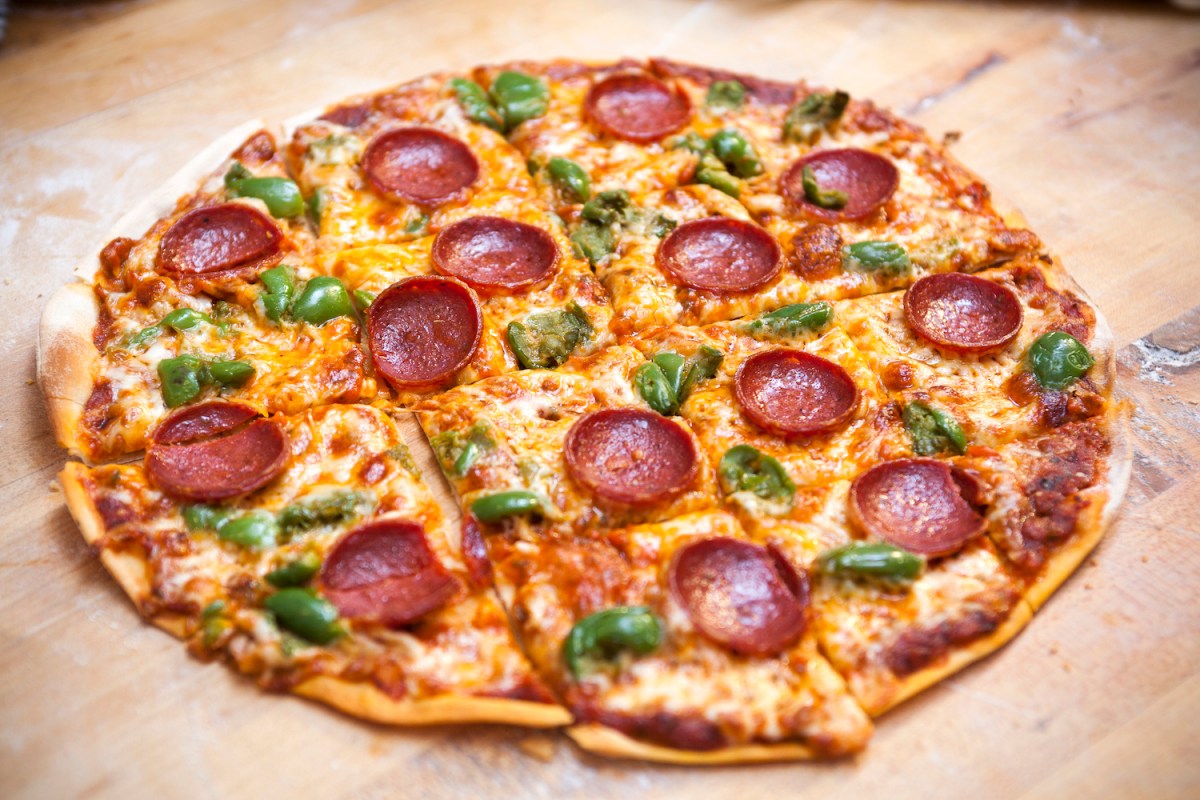 A square cut, thin crust, pepperoni and green pepper cheese pizza on a butcher block surface