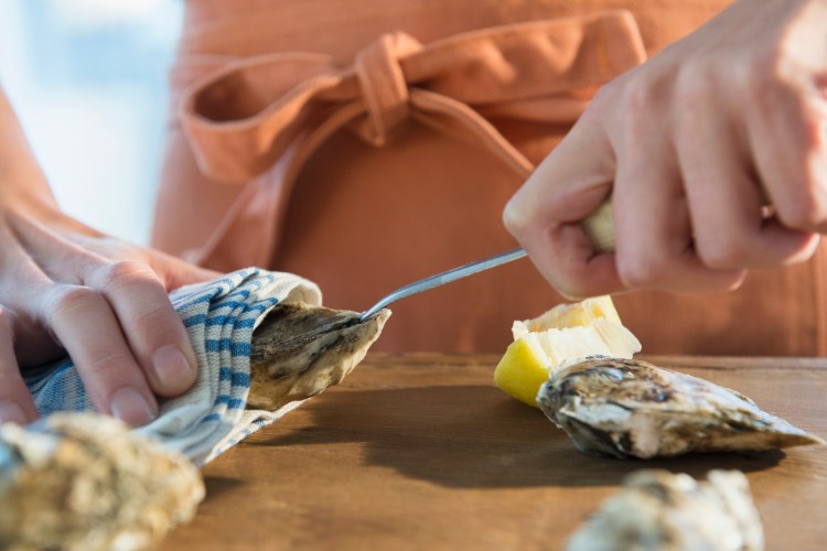 Woman in an orange apron shucking oysters