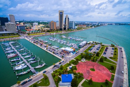 Corpus Christi Texas Aerial Over Marina With a Circle pattern on the T-head and Sailboats and Yatch's on the marina on an amazing day with the CCTX skyline cityscape background and the Harbor Bridge in the distance. Coastal Small Town Paradise vibe.