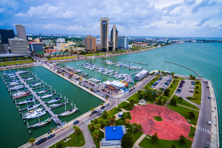 Corpus Christi Texas Aerial Over Marina With a Circle pattern on the T-head and Sailboats and Yatch's on the marina on an amazing day with the CCTX skyline cityscape background and the Harbor Bridge in the distance. Coastal Small Town Paradise vibe.