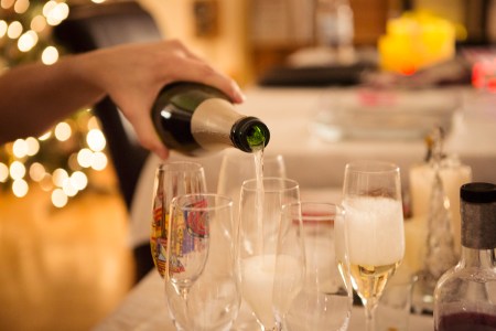 Adult pouring champagne into drinking glasses at a house party