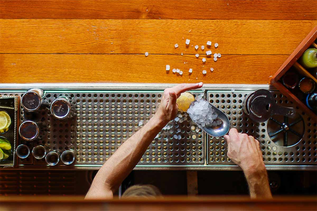 A bartender pouring pebbled ice into a glass on a bar counter. A viral TikTok trend of asking for "less ice" will only hurt your drink.