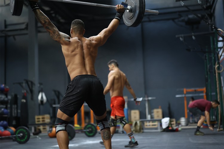 A muscular man lifting a barbell over his head. Here's how strength training can actually give you youthful skin.