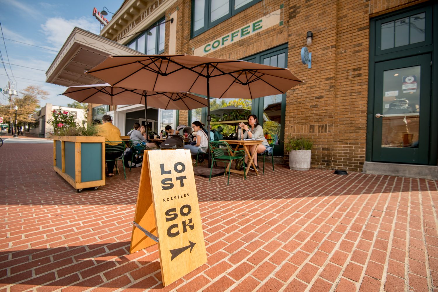 sign outside, beige umbrellas, woman sitting down at table