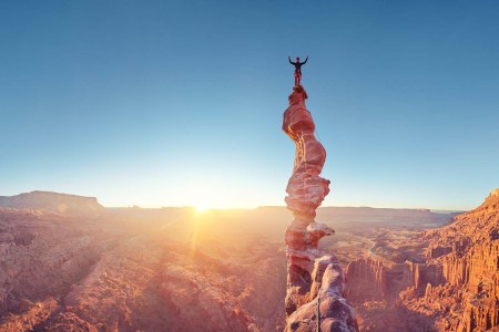 Rock climber celebrating on top of summit of climb at sunset