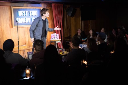 Man talking on a stage under a spotlight to a crowd of people, one of the places to see comedy in New York