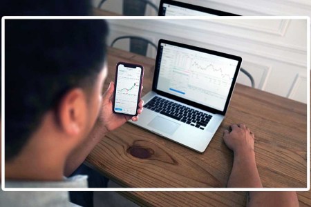 A man looking at stocks on his phone and laptop