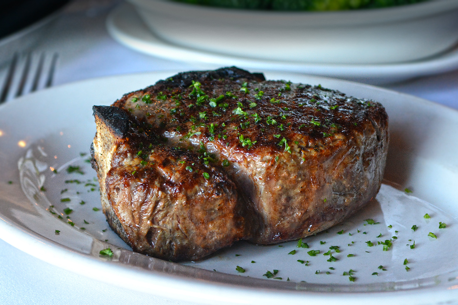 a bone-in filet mignon steak topped with parsley on a white plate