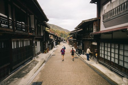 Runners on a quiet road in the Japanese Alps, running past shop keepers.