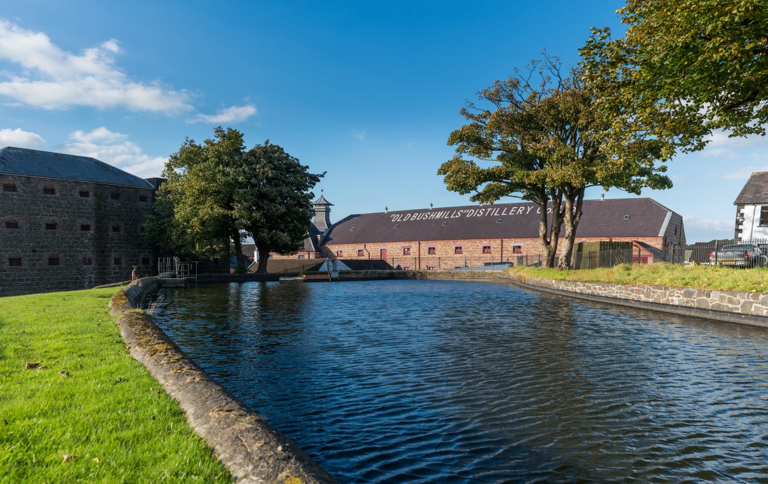 body of water, grass, and trees in front of distillery 