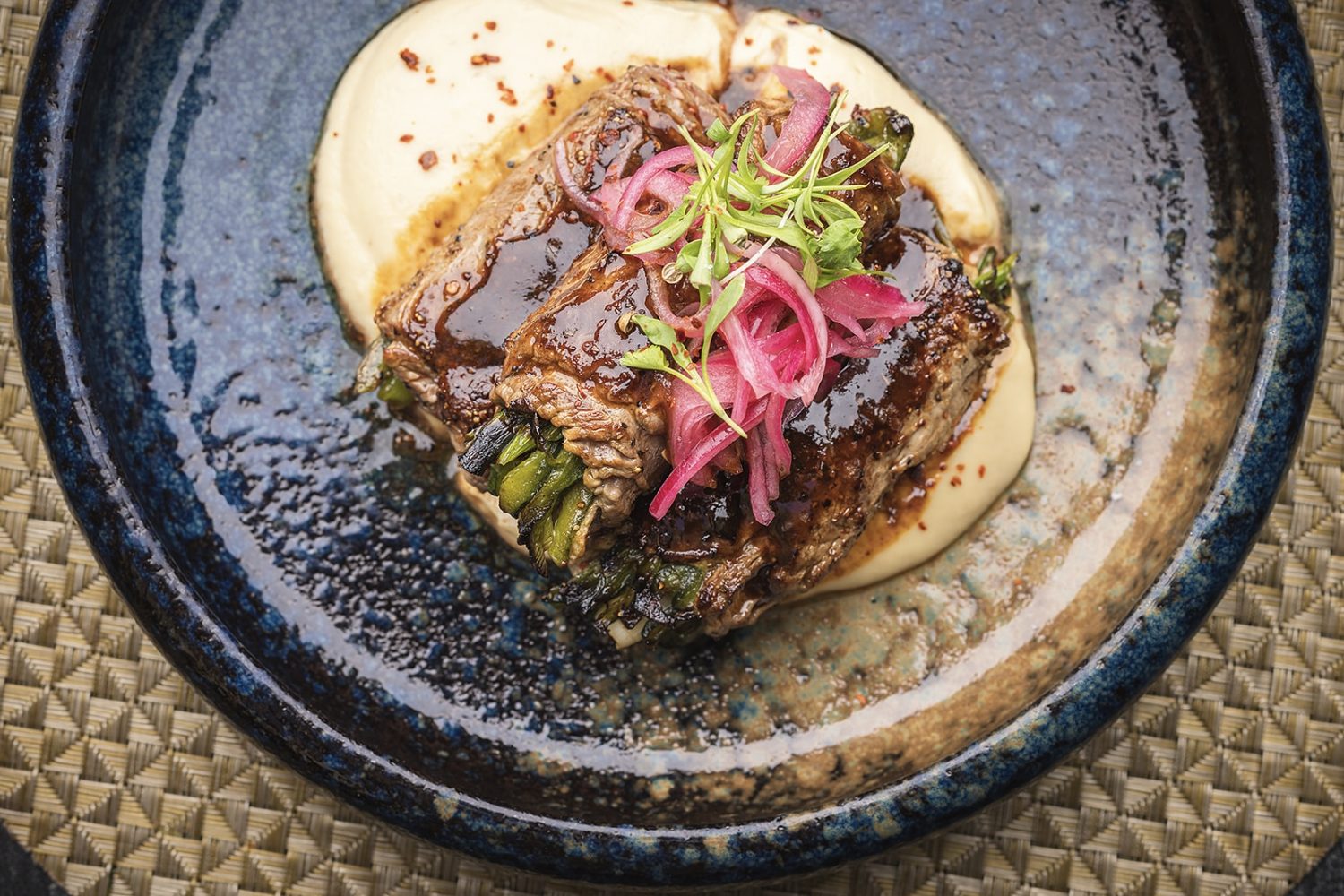 vegetables rolled in beef on top of white cream, garnish on top