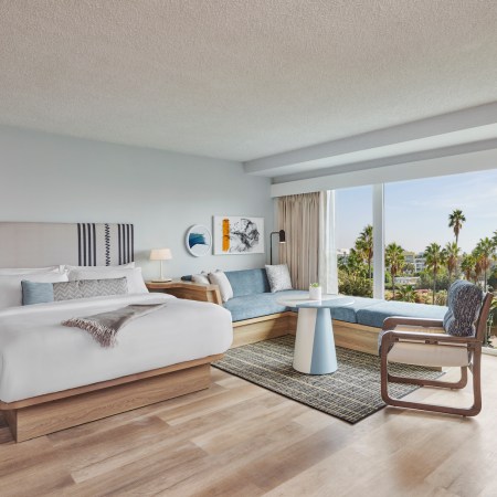 Hotel room with a bed, furniture and floor-to-ceiling windows with a view of palm trees and beach