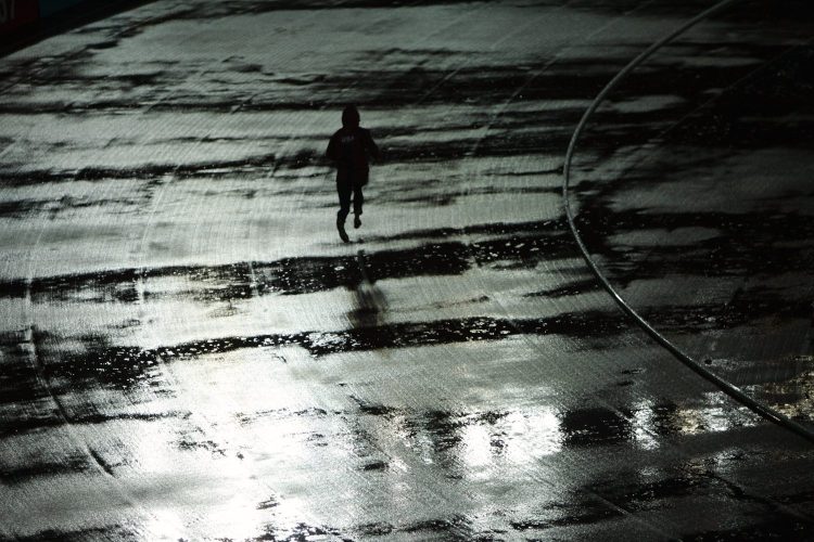 A man running on a rainy track at night.