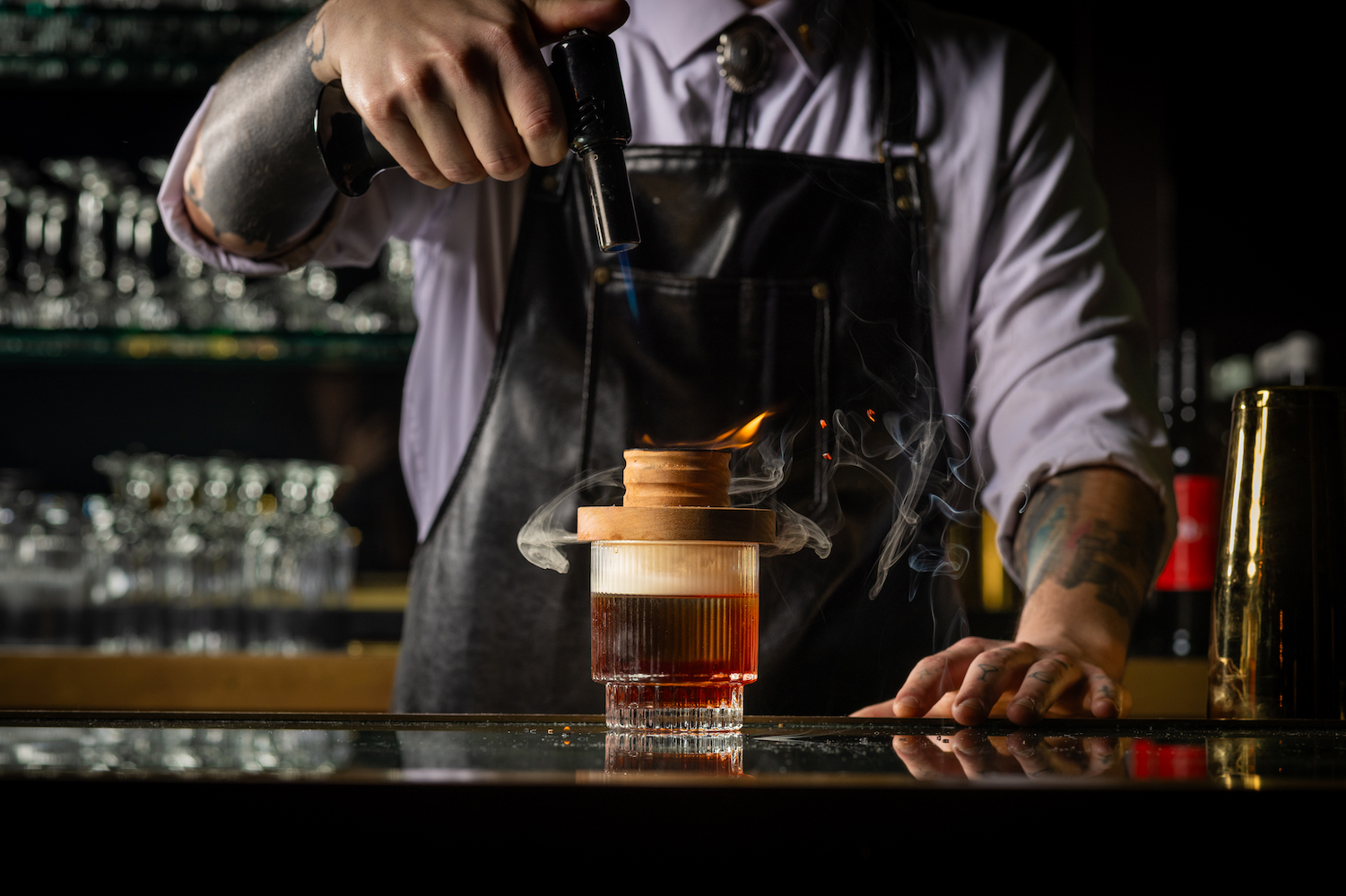 a bartender smoking a cocktail in a rocks glass