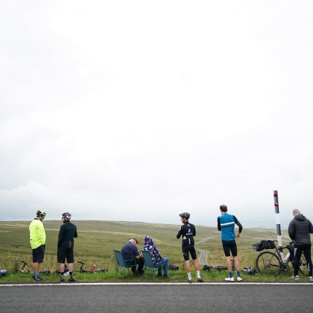 A group of adult men and women standing with bikes and chairs on the side of the road.