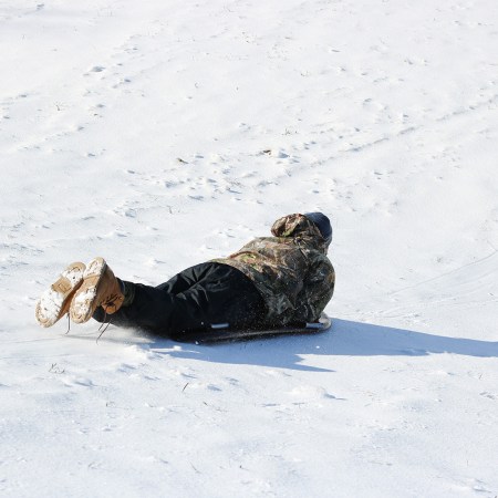 An adult in a camo winter jacket sledding down a hill.