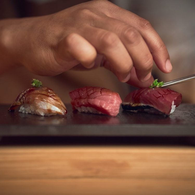 hand places garnish on three pieces of sushi