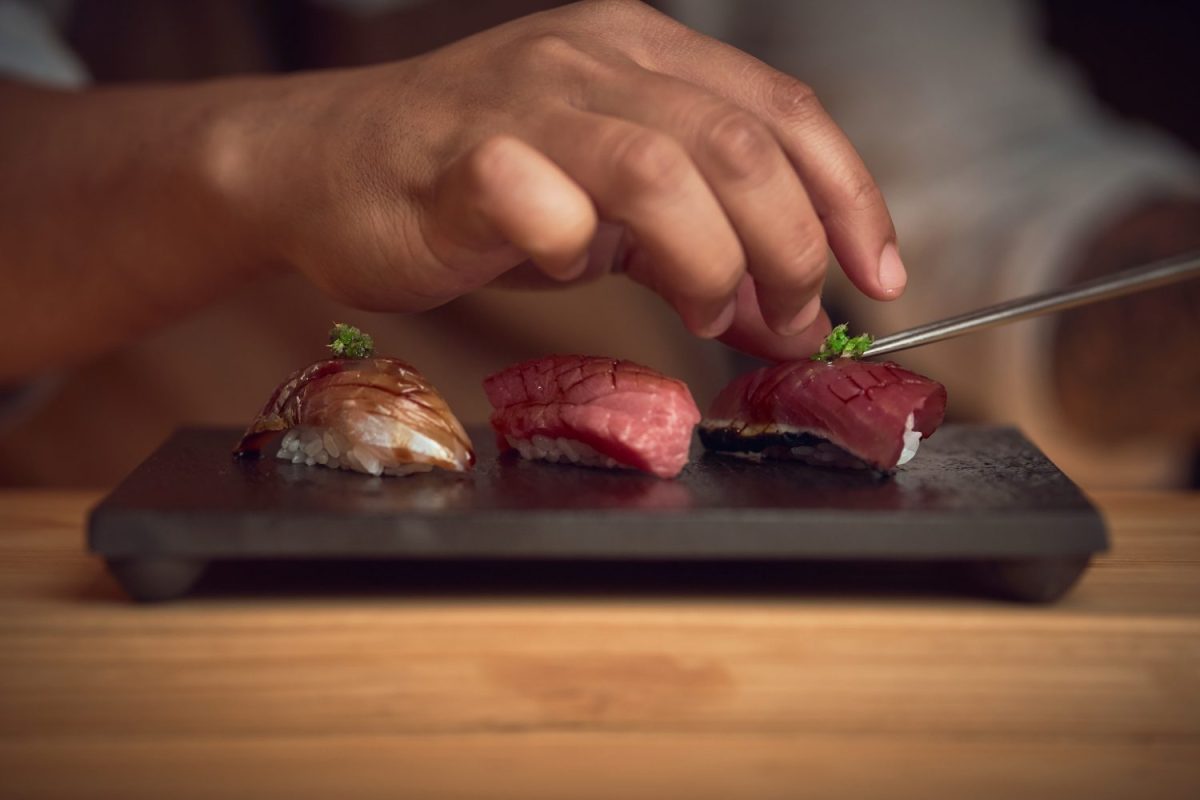 hand places garnish on three pieces of sushi