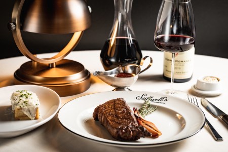 Steak on a plate with gravy and wine on a white tablecloth