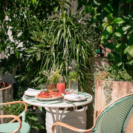 plants in background, green chairs, table, red drink, bagels with lox and capers, utensils