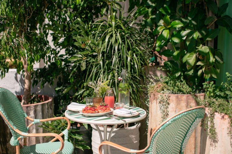 plants in background, green chairs, table, red drink, bagels with lox and capers, utensils