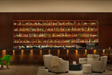 A large dark bar area with an incredibly wide bar rack with dim lighting and a seating area in front of the bar