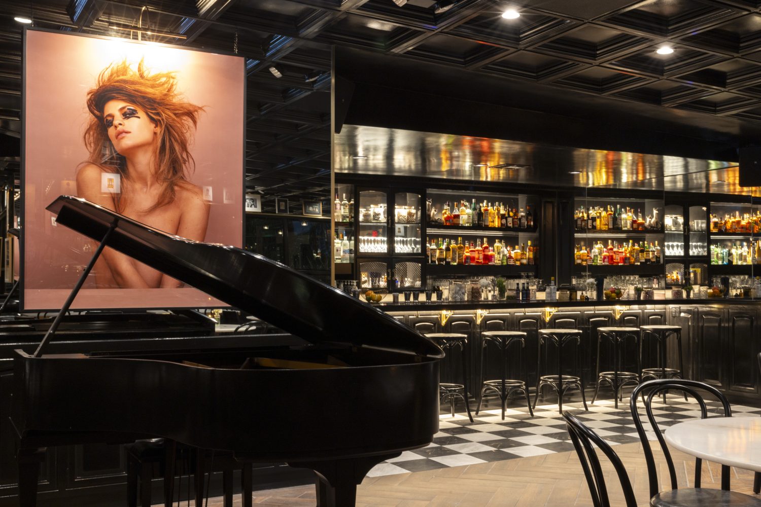 photo of model on wall, liquor on shelves, grand piano