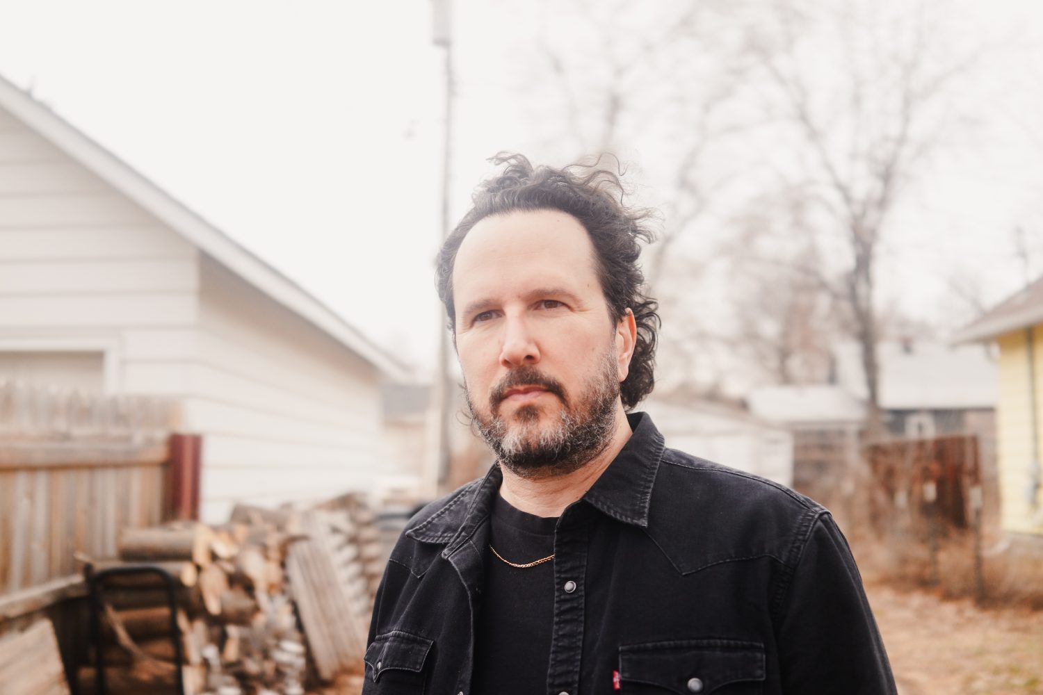 man with goatee in front of white house and wood