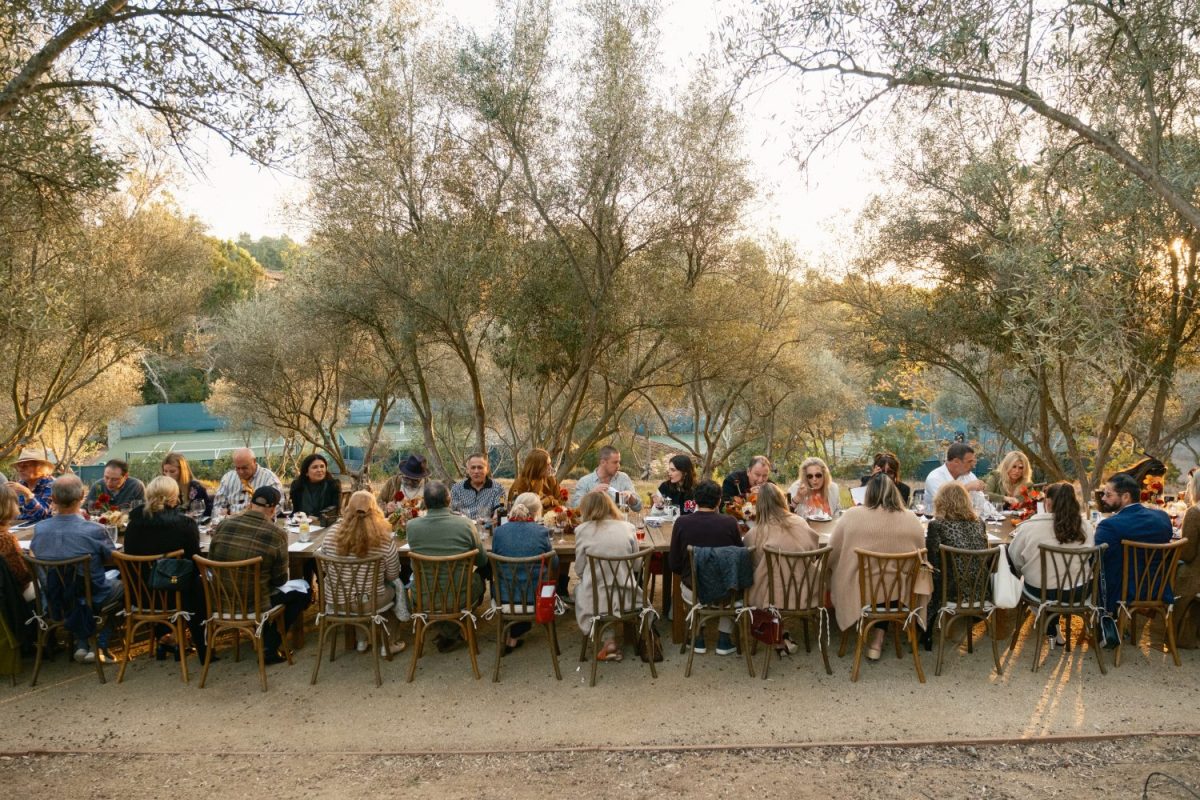 people sitting down at table eating, trees and tennis court in background