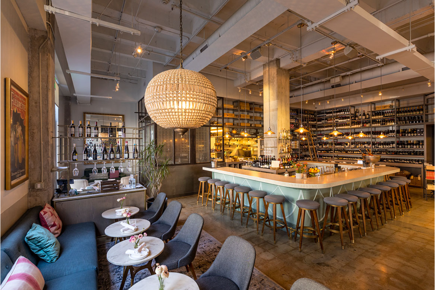 bar with stools, lantern hanging from ceiling, sofa with pillows and tables with flowers on them, wine everywhere