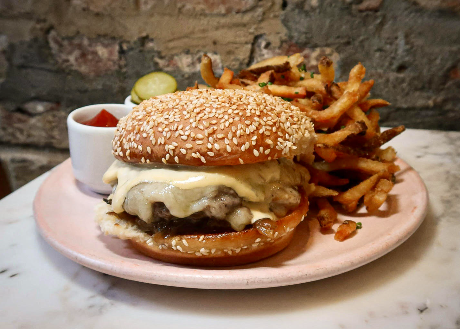 burger with sesame bun and cheese, pickles and french fries on the side