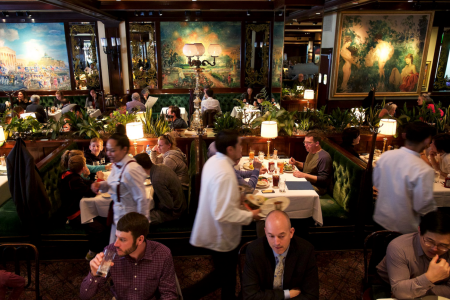 families sitting at green booths, waiters moving, people sitting at the bar, three big paintings