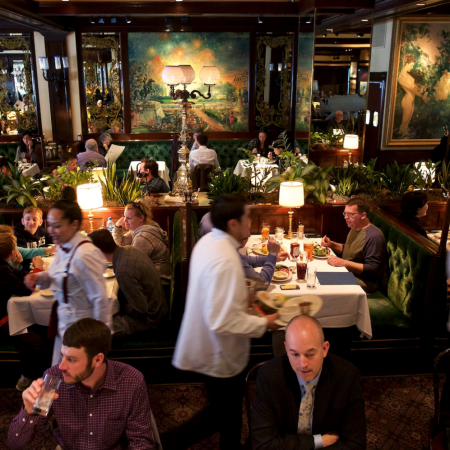 families sitting at green booths, waiters moving, people sitting at the bar, three big paintings