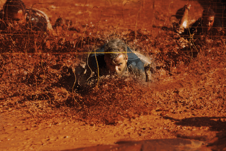 An image of men crawling through mud under live wires during a Tough Mudder event. We take a look at what happened to the king of obstacle course races.